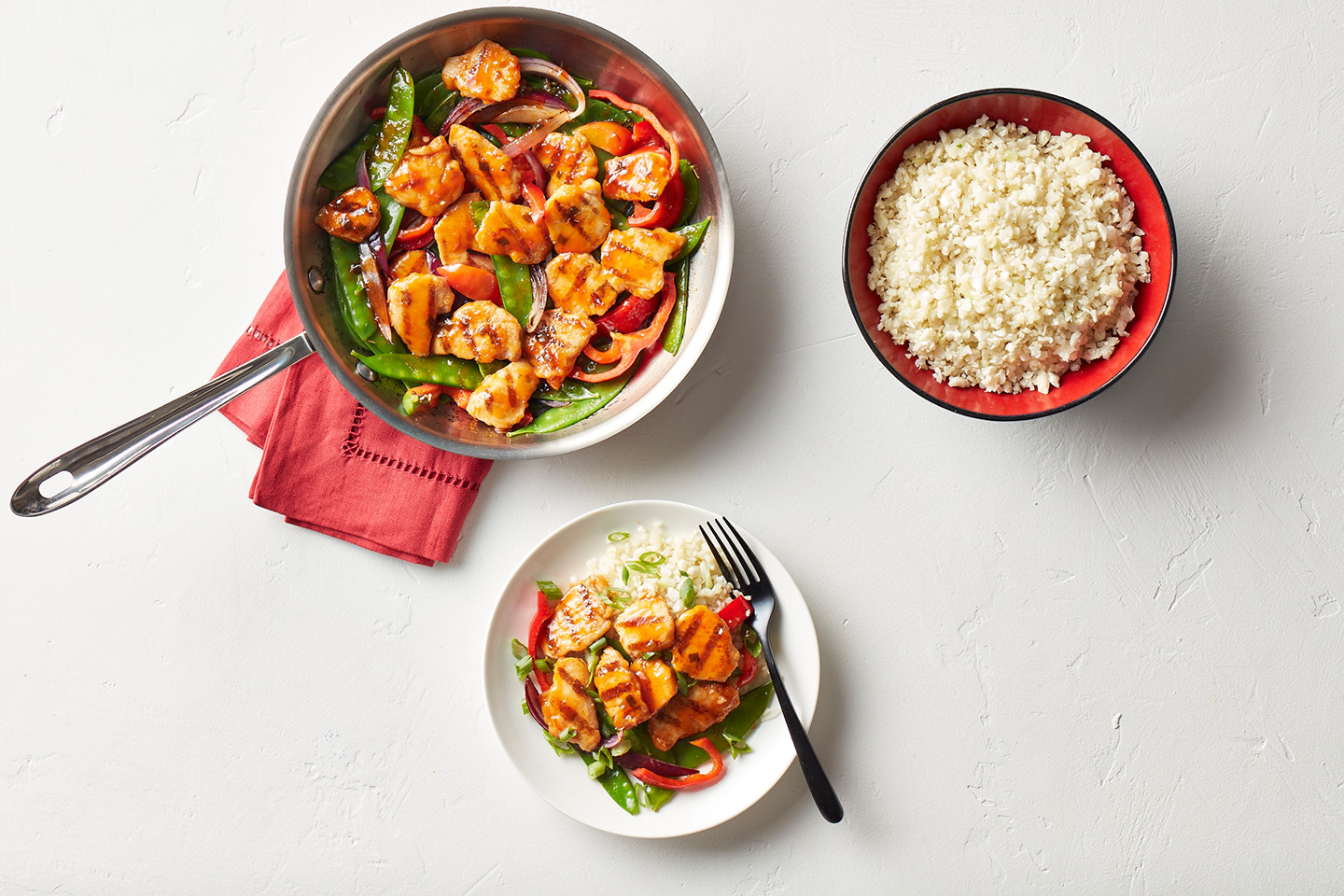 A pan of stir-fried chicken with snap peas, bell peppers, and red onions, served with a side of rice.