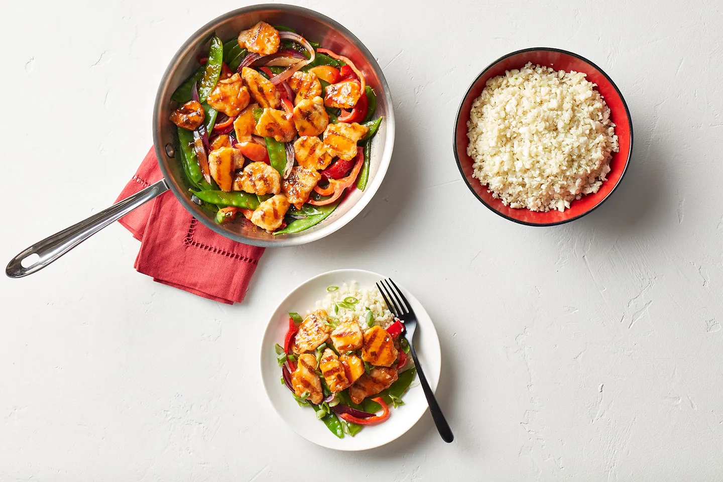 A pan of stir-fried chicken with snap peas, bell peppers, and red onions, served with a side of rice.