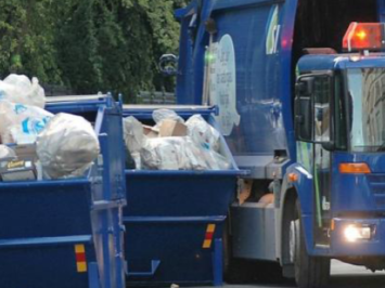Garbage truck parked next to two trash filled dumpsters