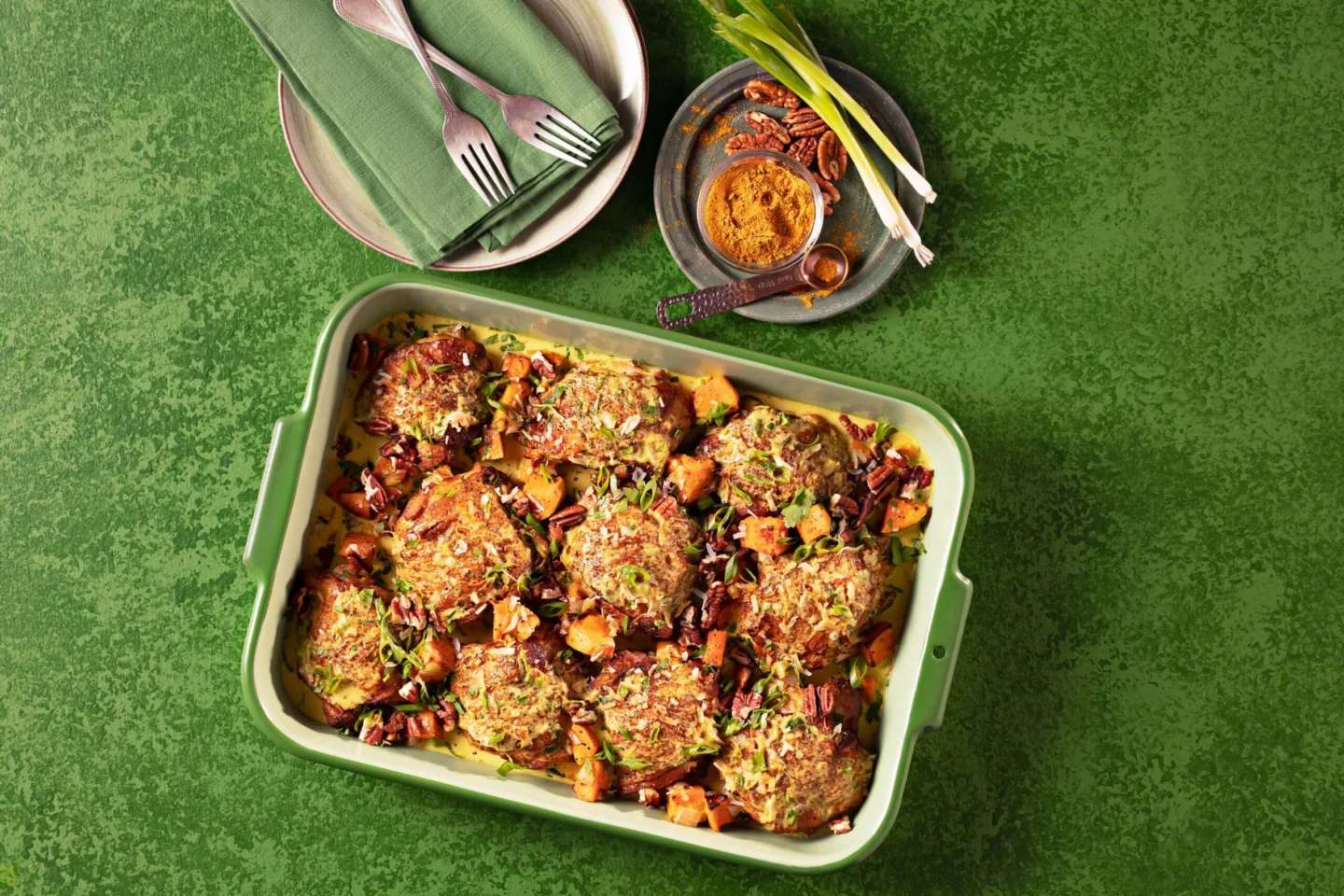 A green baking dish filled with Carribean jerk chicken thighs topped with pecans, green onions, and diced sweet potatoes.