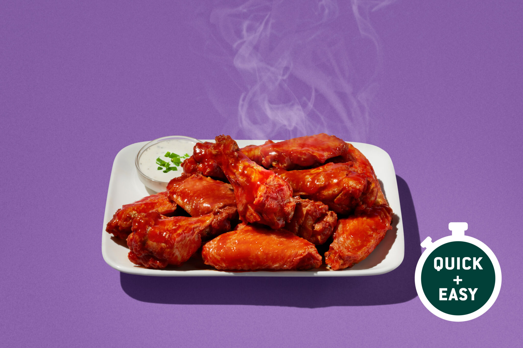A steaming plate of buffalo chicken wings coated in a glossy sauce, served with ranch dressing.