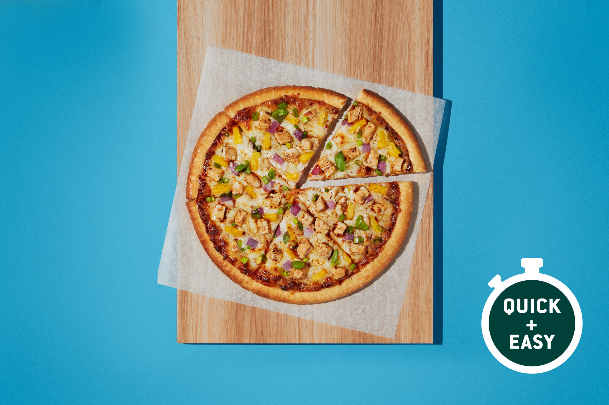 A freshly baked BBQ chicken pizza with diced chicken, bell peppers, and red onions on a wooden cutting board.